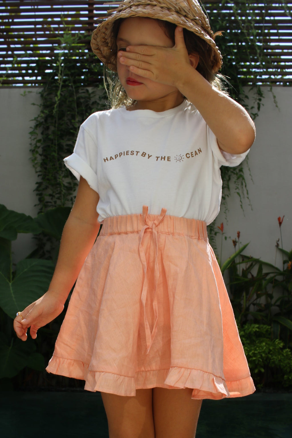 Person wearing a peach skirt and white top with text, standing outdoors.