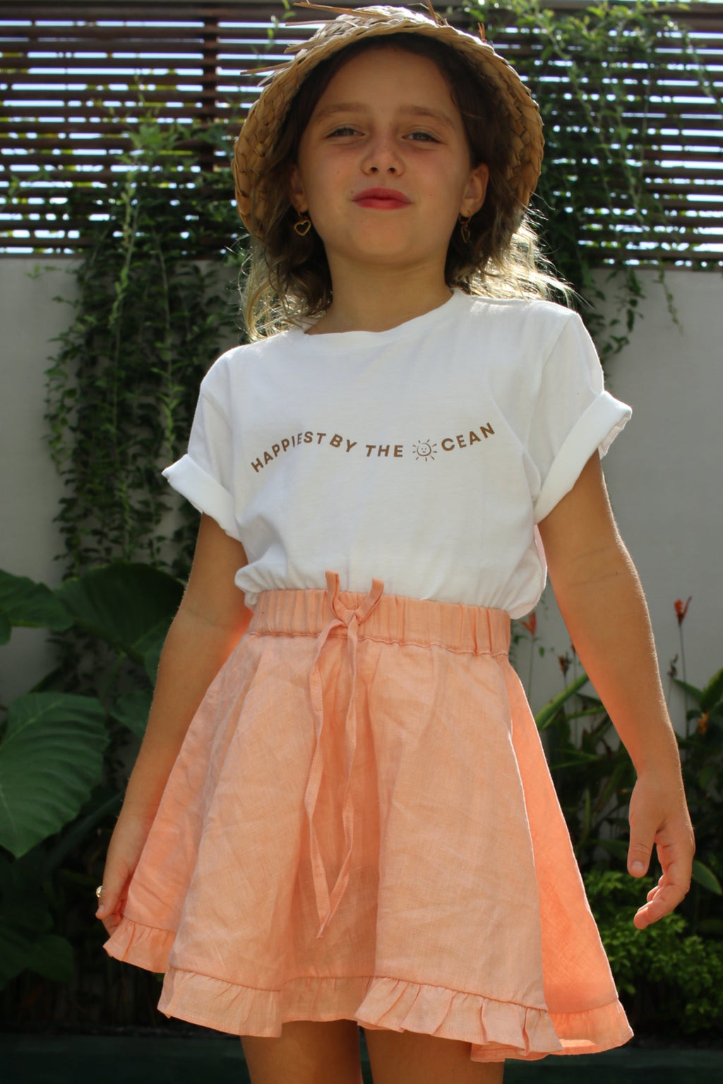 Person wearing a peach skirt and white top outdoors with greenery in the background