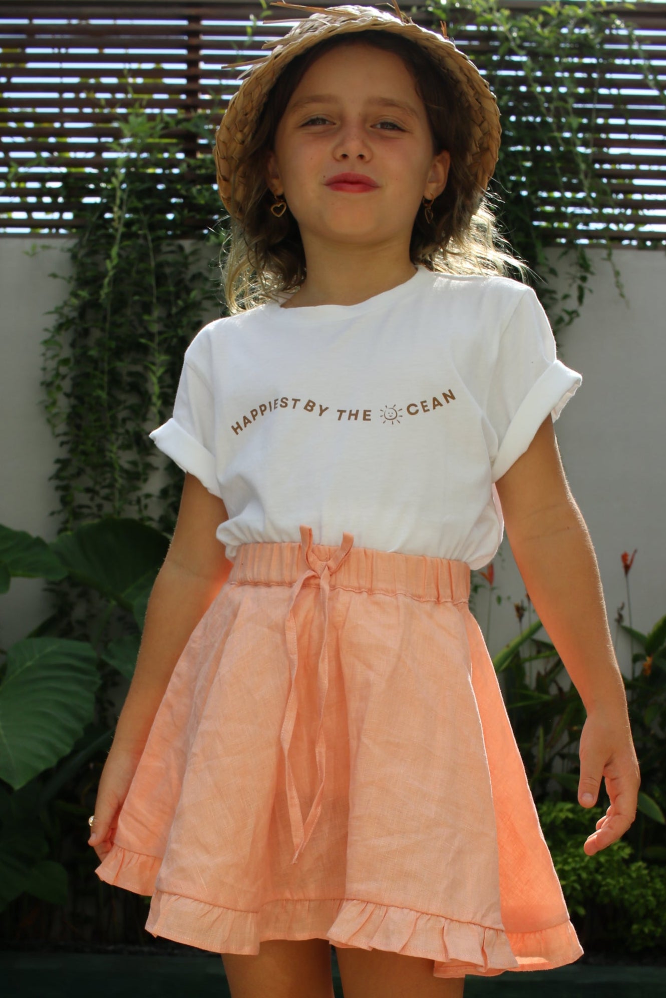 Person wearing a peach skirt and white top outdoors with greenery in the background