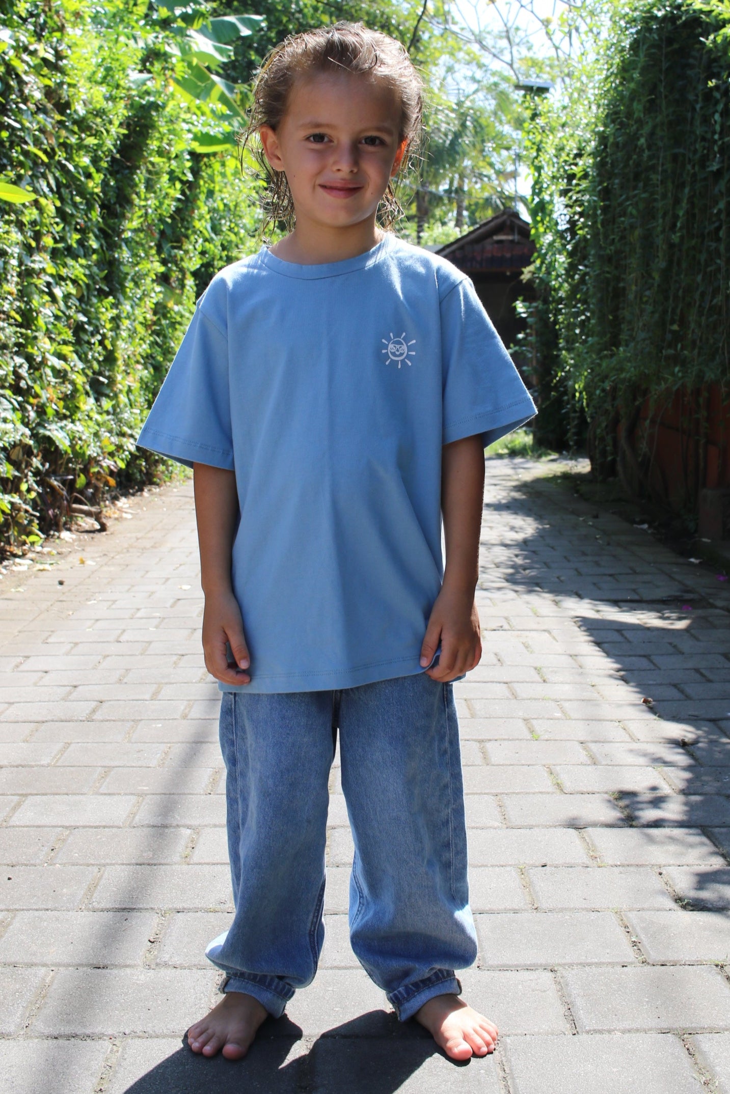 Child in a blue shirt standing on a paved path with greenery in the background