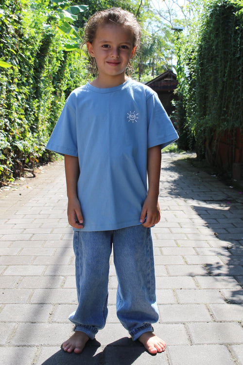 Child in a blue shirt standing on a paved path with greenery in the background