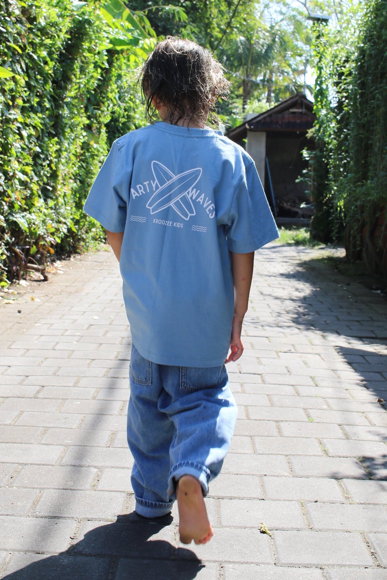 Person in a blue hoodie walking on a paved path with greenery on the side
