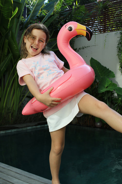 Person holding a pink flamingo-shaped pool float with greenery in the background